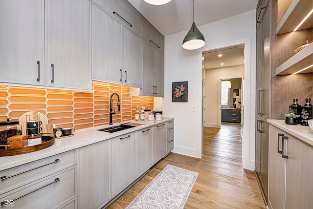 kitchen with light wood-type flooring, light stone counters, decorative light fixtures, and sink