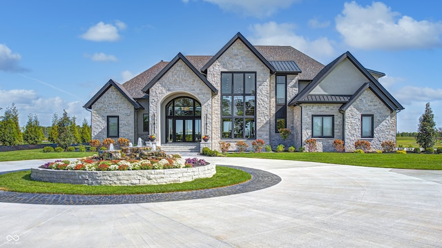 french country inspired facade featuring a standing seam roof, a front lawn, curved driveway, and metal roof