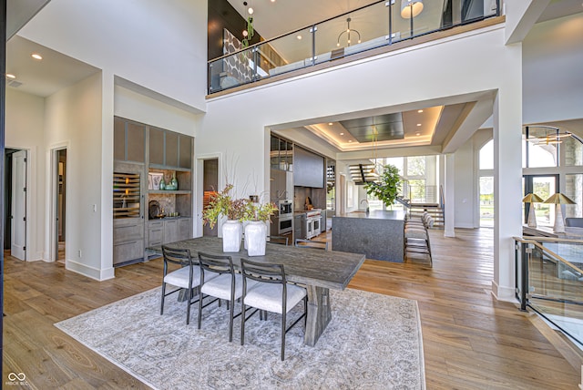 dining room with light wood-type flooring, a raised ceiling, and a high ceiling