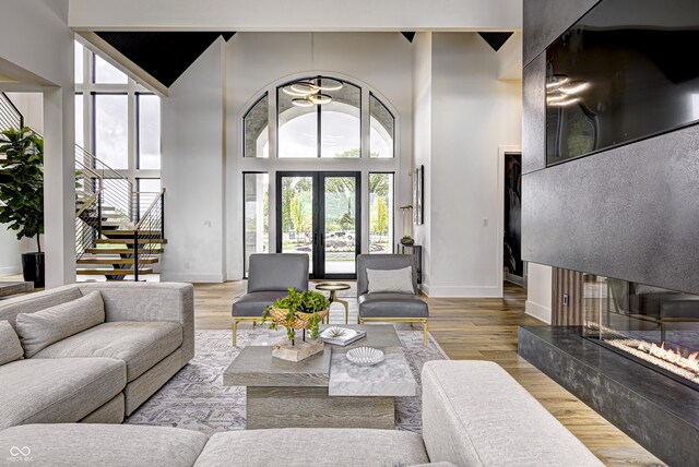 living room with a premium fireplace, light hardwood / wood-style flooring, a high ceiling, ceiling fan, and french doors