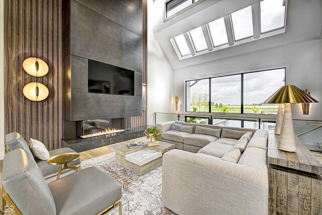 living room featuring a skylight, light hardwood / wood-style floors, high vaulted ceiling, and a large fireplace