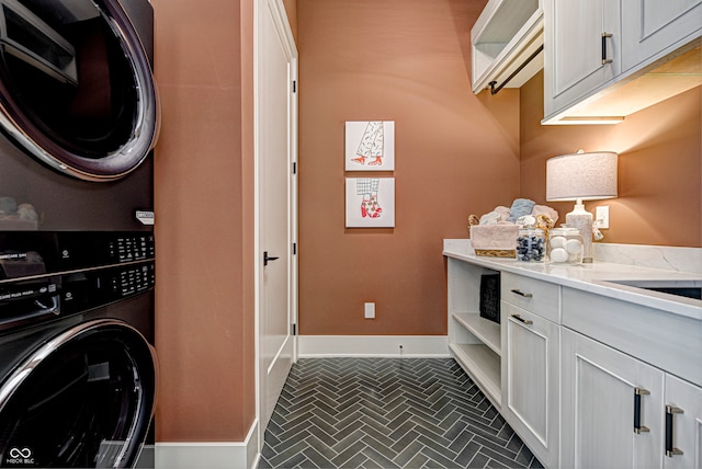 clothes washing area with stacked washer / dryer, dark tile patterned floors, and cabinets