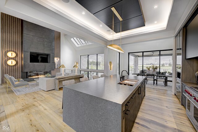 kitchen featuring a raised ceiling, sink, a kitchen island with sink, a fireplace, and light wood-type flooring