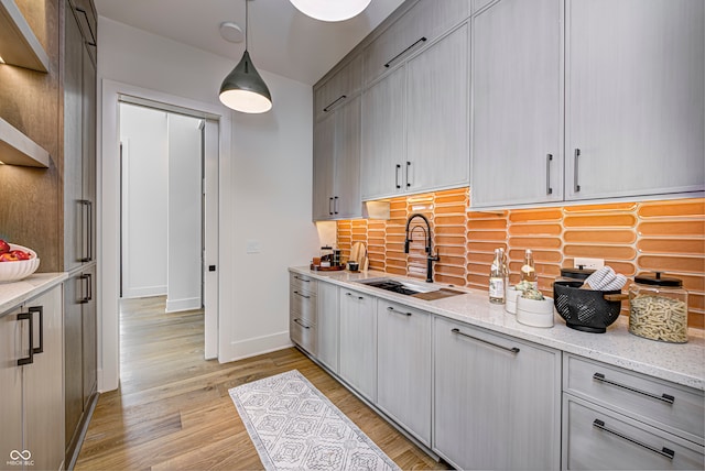 kitchen featuring light stone counters, decorative light fixtures, light wood-type flooring, and sink