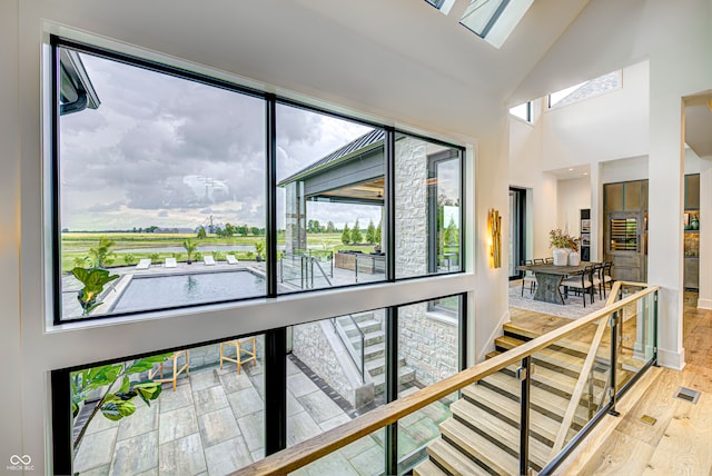 corridor with hardwood / wood-style floors, high vaulted ceiling, a skylight, and plenty of natural light