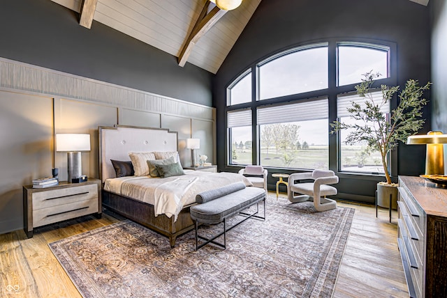 bedroom with wood-type flooring, multiple windows, and beamed ceiling