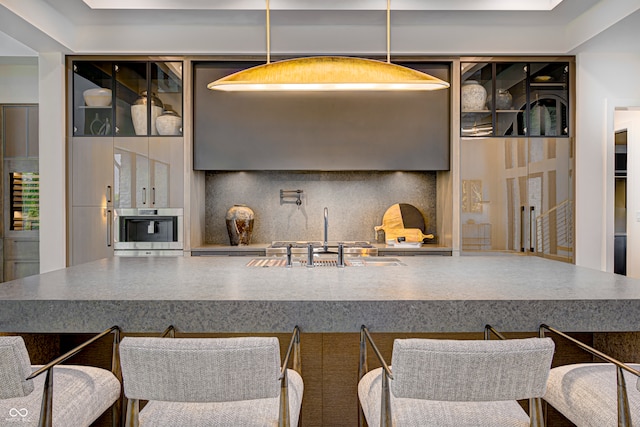 kitchen with decorative light fixtures, sink, stainless steel oven, and decorative backsplash