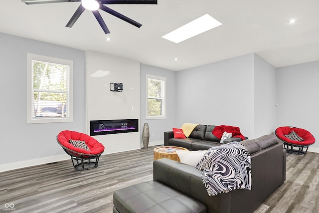 living room featuring a skylight, wood-type flooring, and ceiling fan