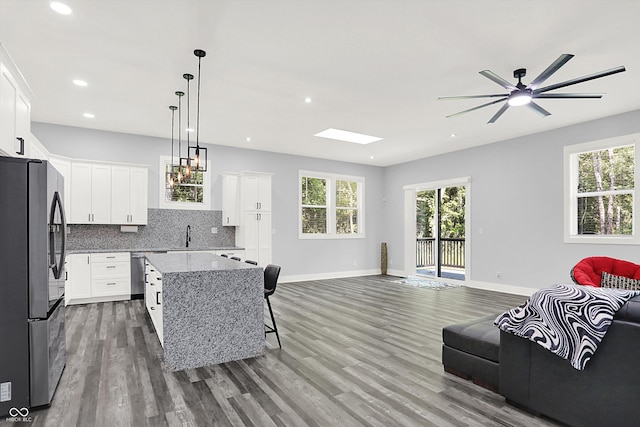 kitchen featuring wood-type flooring, decorative backsplash, a center island, light stone counters, and appliances with stainless steel finishes