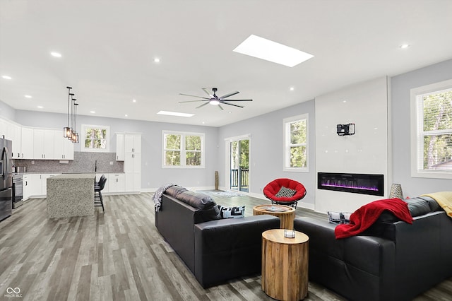 living room with light hardwood / wood-style floors, ceiling fan, and a skylight