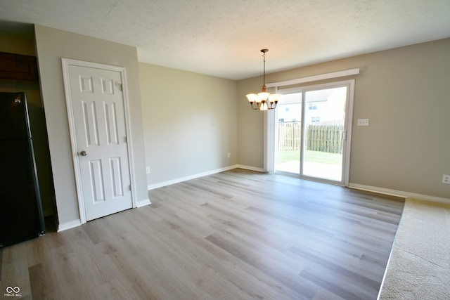 spare room featuring a textured ceiling, a chandelier, and light hardwood / wood-style floors