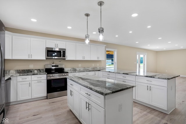 kitchen with appliances with stainless steel finishes, hanging light fixtures, white cabinets, and light hardwood / wood-style floors