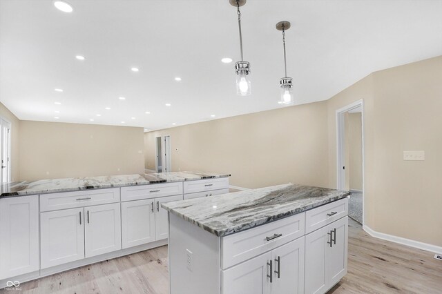 kitchen featuring light stone countertops, white cabinets, light hardwood / wood-style floors, pendant lighting, and a center island