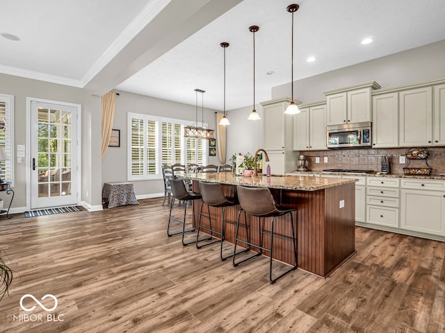 kitchen with a kitchen bar, appliances with stainless steel finishes, backsplash, stone countertops, and wood-type flooring