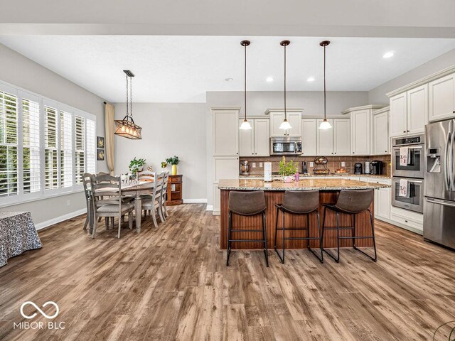 kitchen with light stone counters, appliances with stainless steel finishes, decorative backsplash, hardwood / wood-style flooring, and decorative light fixtures