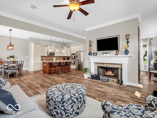 living room with crown molding, a tile fireplace, light hardwood / wood-style flooring, and ceiling fan