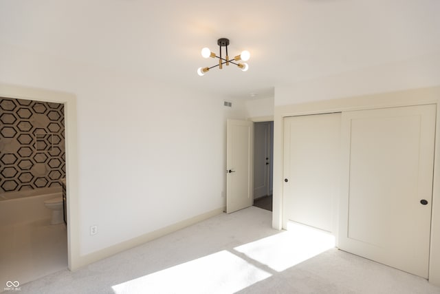 unfurnished bedroom featuring a closet, ensuite bath, light colored carpet, and a chandelier