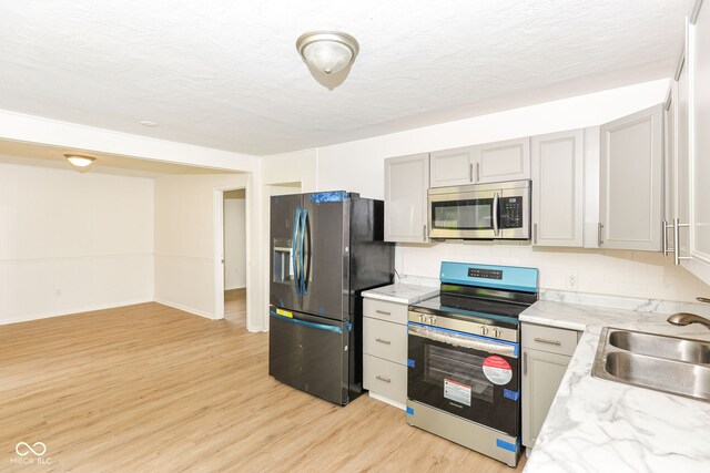 kitchen with tasteful backsplash, light wood-type flooring, sink, appliances with stainless steel finishes, and gray cabinetry