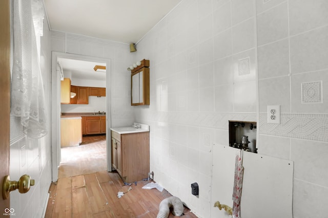 hallway featuring light hardwood / wood-style floors, sink, crown molding, and tile walls