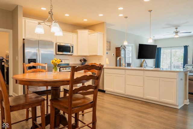 kitchen with pendant lighting, white cabinetry, appliances with stainless steel finishes, and light hardwood / wood-style floors