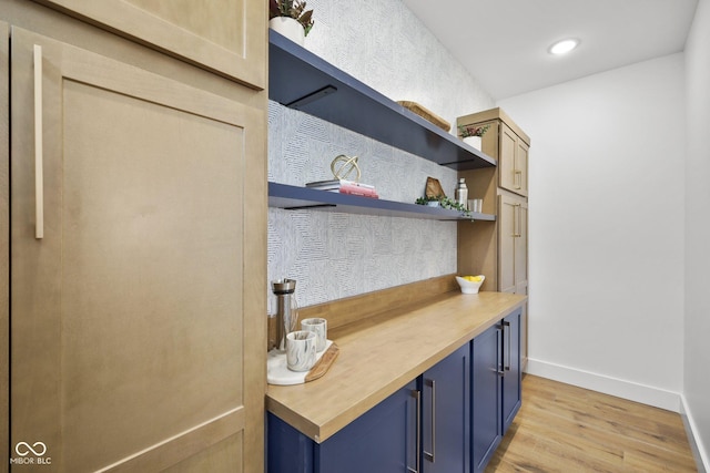 bar with blue cabinetry, butcher block countertops, and light hardwood / wood-style flooring