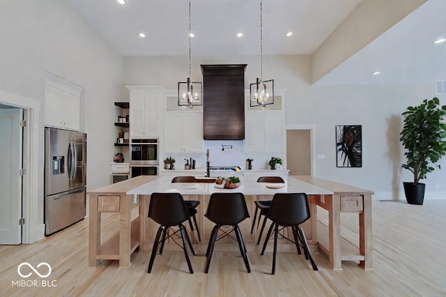 kitchen with white cabinetry, light wood-type flooring, an island with sink, appliances with stainless steel finishes, and pendant lighting