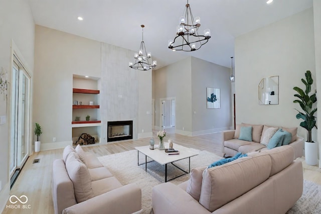 living room with a notable chandelier, light wood-type flooring, a high ceiling, built in features, and a large fireplace