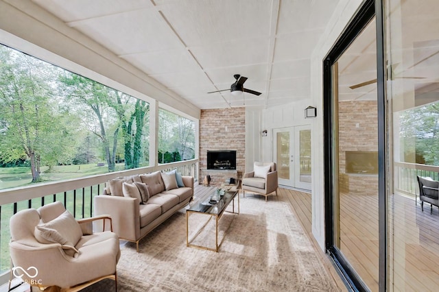 sunroom / solarium with a stone fireplace, a wealth of natural light, ceiling fan, and french doors