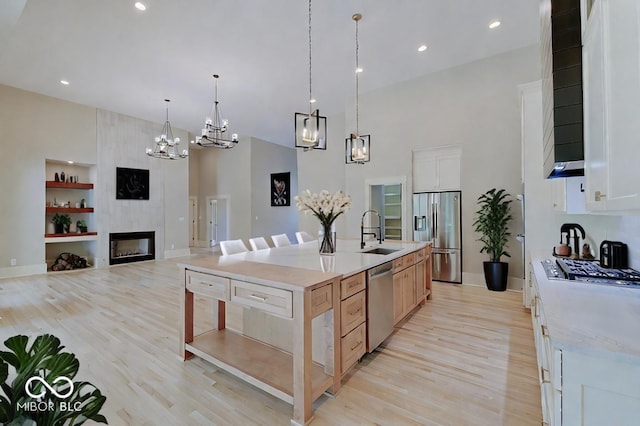 kitchen with white cabinets, stainless steel appliances, light stone counters, light wood-type flooring, and a large island with sink