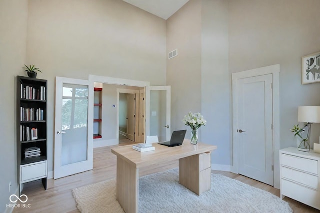 office area featuring a towering ceiling and light hardwood / wood-style flooring