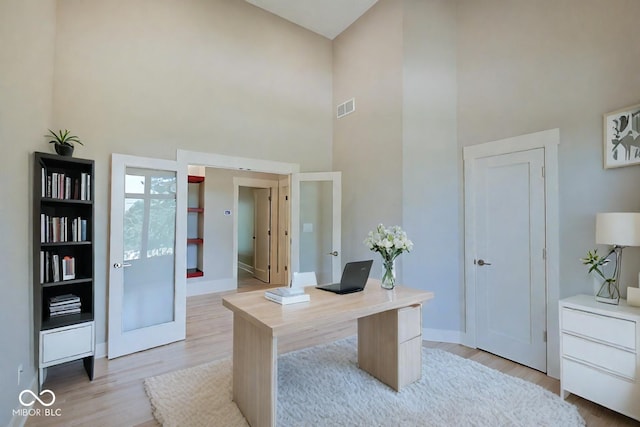 office with baseboards, visible vents, a high ceiling, french doors, and light wood-type flooring