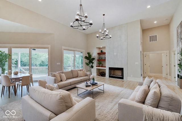 living room featuring a large fireplace, a notable chandelier, a high ceiling, light wood-type flooring, and built in features