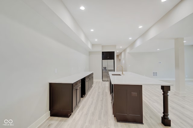 kitchen with stainless steel fridge with ice dispenser, sink, a center island with sink, dark brown cabinetry, and light hardwood / wood-style flooring