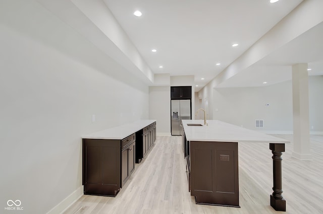 kitchen featuring visible vents, an island with sink, light countertops, stainless steel refrigerator with ice dispenser, and a sink