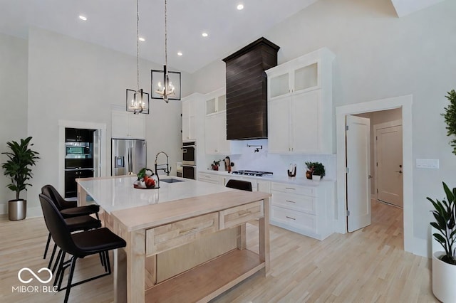 kitchen with decorative light fixtures, stainless steel appliances, light countertops, a center island with sink, and glass insert cabinets