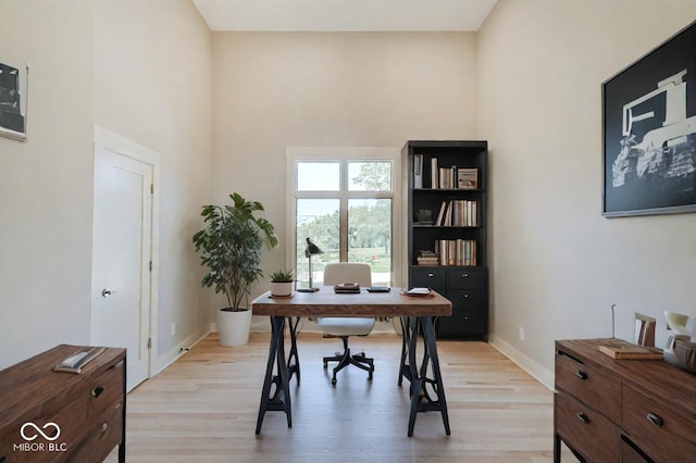 office featuring light wood-type flooring, a towering ceiling, and baseboards
