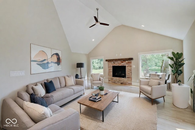 living room featuring high vaulted ceiling, a fireplace, light wood-type flooring, and ceiling fan