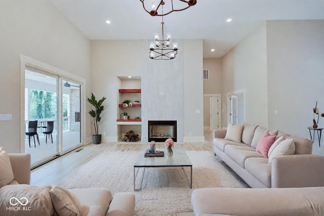 living room featuring a large fireplace, baseboards, a towering ceiling, light wood-style floors, and a chandelier