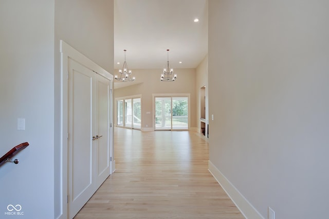 hallway featuring baseboards, a notable chandelier, a towering ceiling, and light wood finished floors