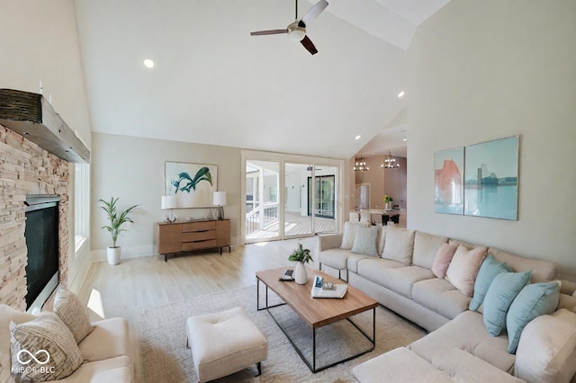 living room featuring high vaulted ceiling, a fireplace, ceiling fan with notable chandelier, and light wood-type flooring