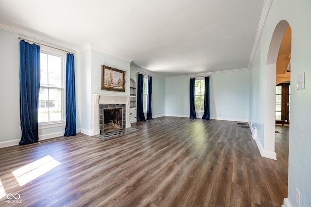 unfurnished living room with dark wood-style floors, arched walkways, a healthy amount of sunlight, and a tiled fireplace