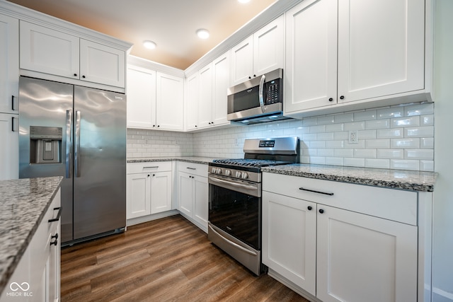 kitchen featuring tasteful backsplash, stainless steel appliances, white cabinets, light stone counters, and dark hardwood / wood-style floors