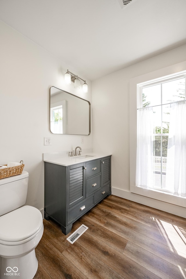 bathroom with toilet, wood finished floors, vanity, visible vents, and baseboards