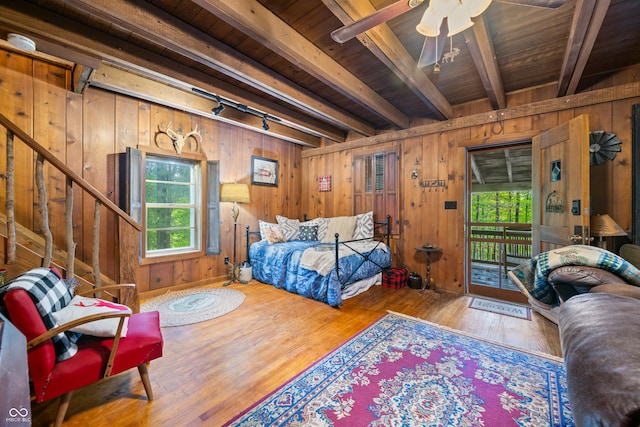 bedroom featuring wood-type flooring, wood walls, beam ceiling, and multiple windows