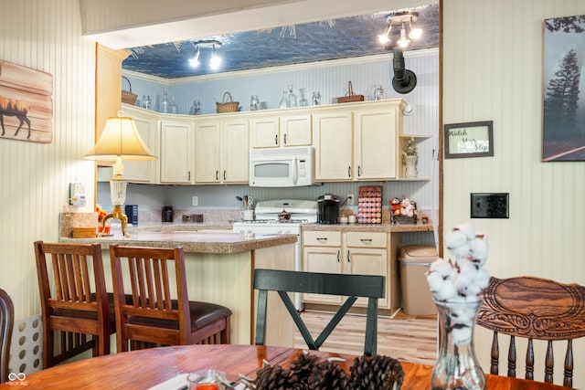 kitchen with white appliances, cream cabinets, light hardwood / wood-style flooring, and decorative light fixtures