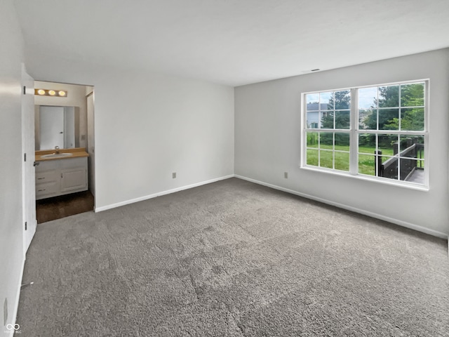 unfurnished bedroom featuring sink, ensuite bathroom, and dark carpet