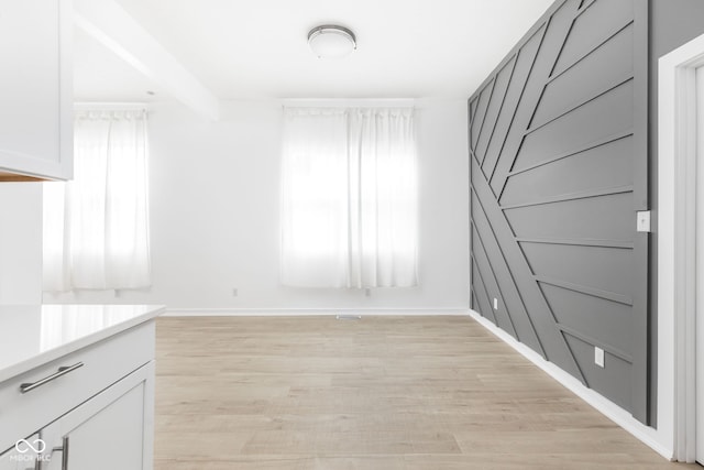 unfurnished dining area with light wood-type flooring and beam ceiling