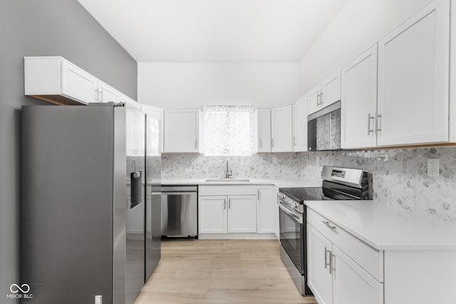 kitchen with appliances with stainless steel finishes, light hardwood / wood-style floors, white cabinetry, backsplash, and sink