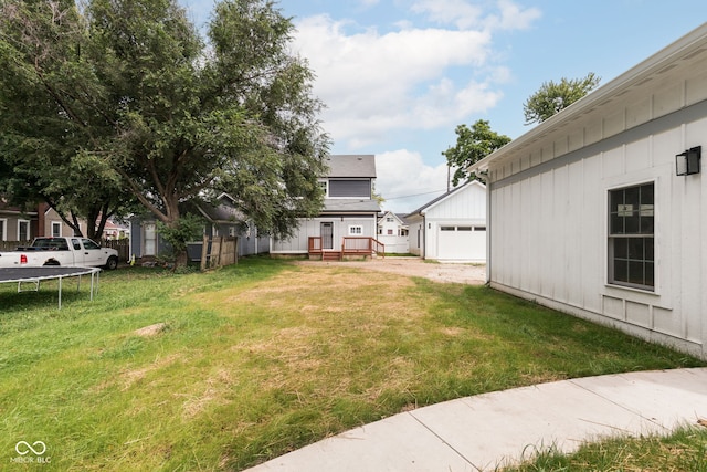 view of yard with a trampoline, a deck, an outdoor structure, and a garage