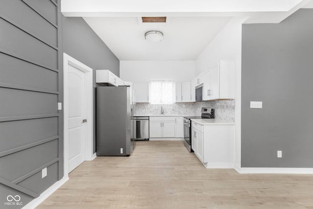 kitchen featuring white cabinets, stainless steel appliances, light wood-type flooring, and tasteful backsplash